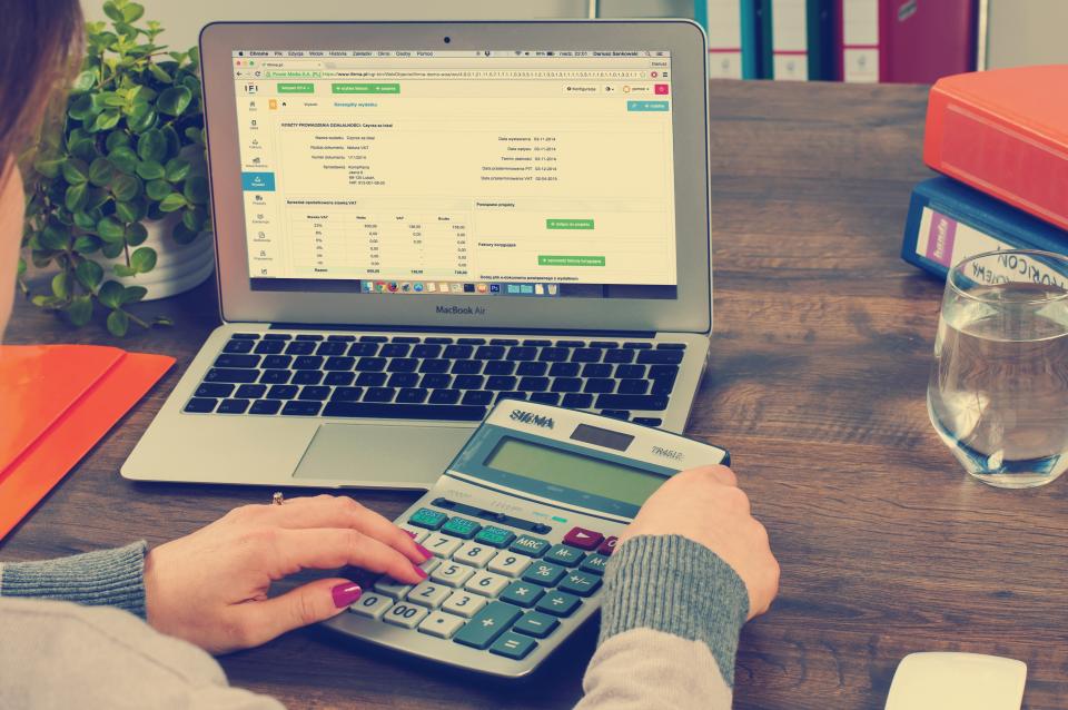 Accountant using a calculator next to a laptop showing financial charts on an office desk
